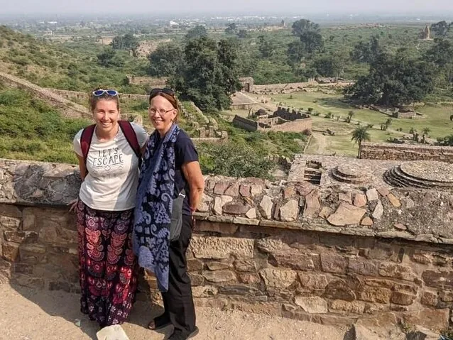 Dos mujeres posando para una foto en un muro de piedra con vistas a las ruinas del Fuerte de Bhangarh