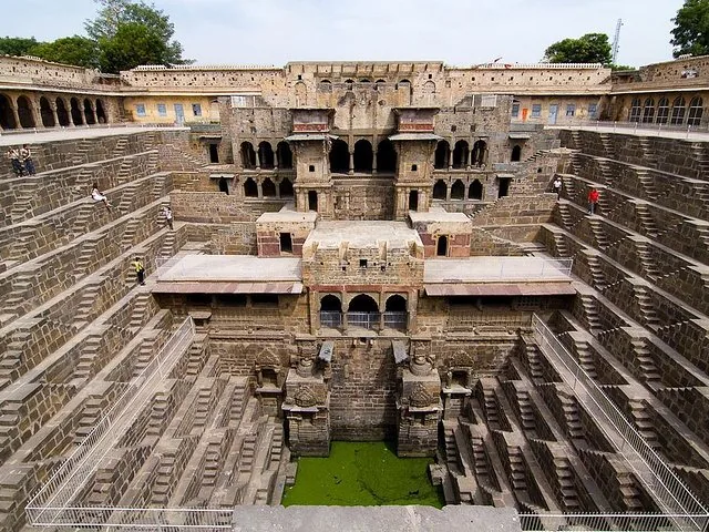 Weitwinkelansicht des Stufenbrunnens Chand Baori mit komplexen Treppen, Wasser und Gebäudestrukturen