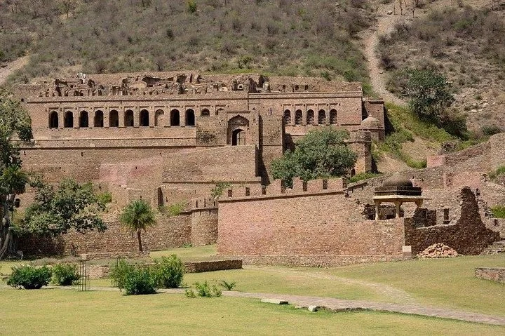 The historical stone structures and walls of Bhangarh Fort surrounded by greenery