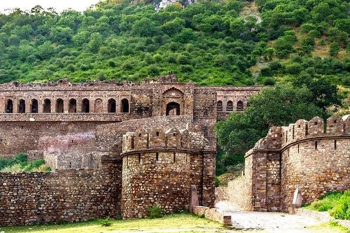 Exterior stone walls and ruins of Bhangarh Fort against a lush green hill