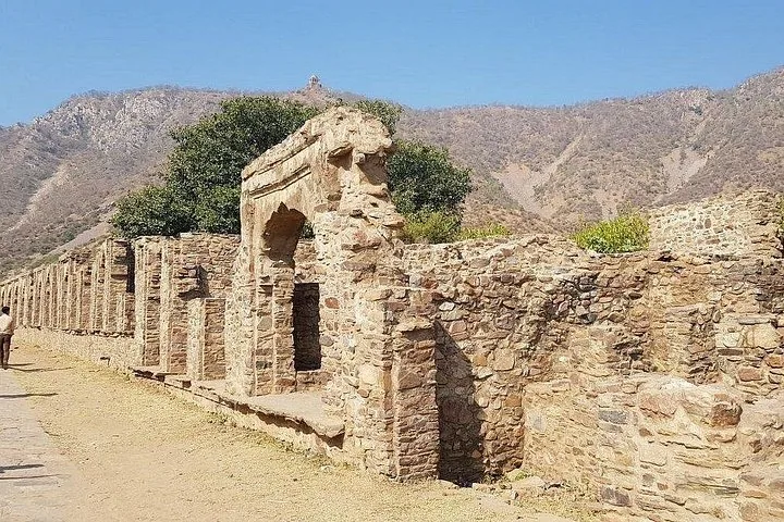 Ruined stone walls and arches forming a path at Bhangarh Fort with mountains behind
