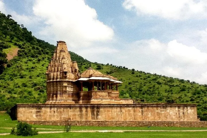 Estructura de un antiguo templo de piedra rodeado de un paisaje cubierto de hierba y una colina verde